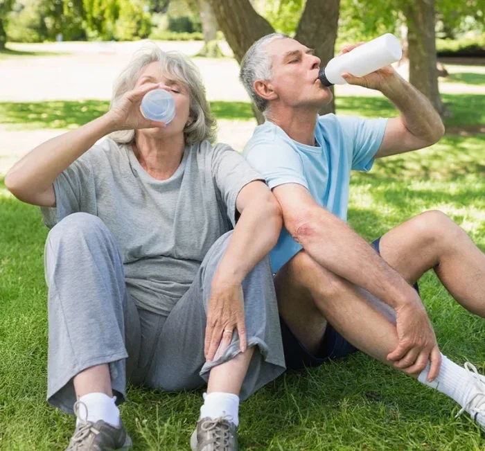 An older couple resting and drinking water outdoors after a walk